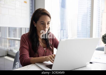 Donna d'affari seria che lavora con un laptop in un moderno edificio alto Foto Stock