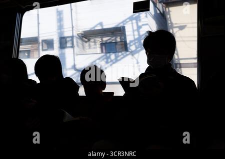 Tutti gli anziani pendolari siedono tranquillamente su un treno, le loro silhouette scure sullo sfondo luminoso degli edifici che passano Foto Stock