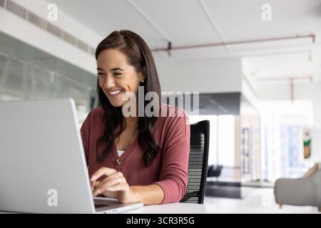 Donna sorridente che lavora su un notebook in ufficio Foto Stock