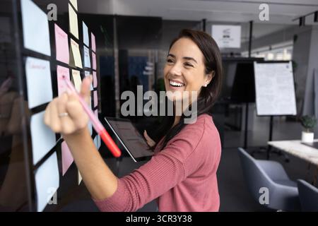 Donna sorridente che scrive note relative alle idee di progetto Foto Stock