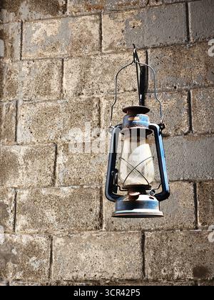 Una vecchia lanterna arrugginita di cherosene è appesa su una parete di mattoni testurizzati, evocando un'atmosfera rustica e vintage Foto Stock