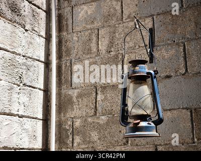 Una vecchia lanterna arrugginita di cherosene è appesa su una parete di mattoni testurizzati, evocando un'atmosfera rustica e vintage Foto Stock