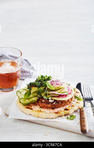 Hamburger vegetariano gourmet su una focaccia con cetriolo a fette, ravanelli e verdure, servito con una bevanda. Foto Stock