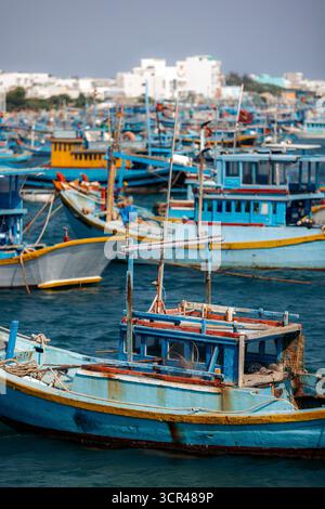 Numerose barche da pesca colorate ancorate in un vivace porto con vista della città lontana. Isola di Phu Quy, B‐ nh Thuan, Vietnam Foto Stock