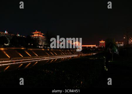 Antiche mura cinesi illuminate di notte, che si riflettono su un fiume tranquillo. XI'an, Cina Foto Stock