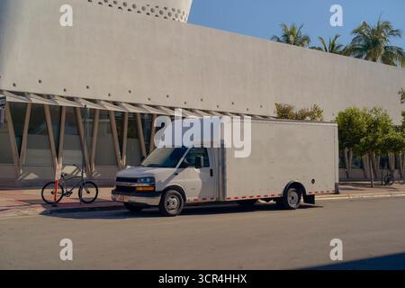 Pulmino bianco parcheggiato su una strada soleggiata accanto a un edificio moderno e biciclette. Miami, Florida, Stati Uniti Foto Stock
