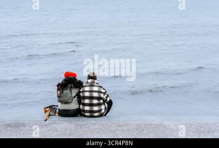 Un uomo e una donna, seduti e affacciati sul mare, sul lungomare di Cleveleys, Lancashire, Regno Unito Foto Stock