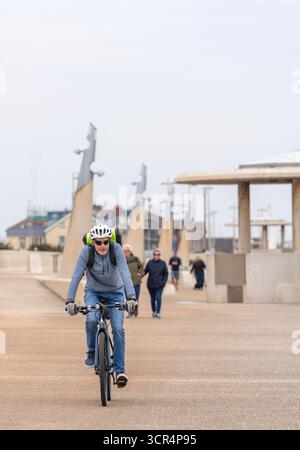 Un uomo che indossa un casco da ciclismo mentre guida la sua bicicletta lungo il lungomare di Cleveleys, Lancashire, Regno Unito Foto Stock