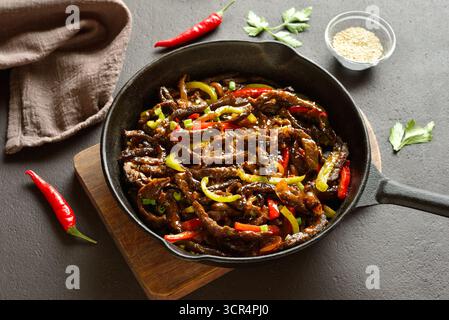 Padella in stile cinese di frittura tagliata a fette sottili a strisce di manzo e peperoni su sfondo marrone scuro. Vista ravvicinata Foto Stock