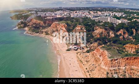 Vista aerea sulla costa dell'Algarve con i droni, acque turchesi dell'oceano, scogliere rocciose, spiaggia sabbiosa, vacanza, resort, edifici cittadini, mare Atlantico, estate Foto Stock