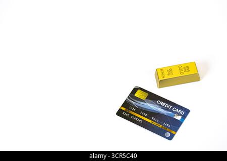 Una carta di credito e una barra d'oro sono collocate su sfondo bianco, simboleggiando ricchezza e concetti finanziari con ampio spazio di copia Foto Stock