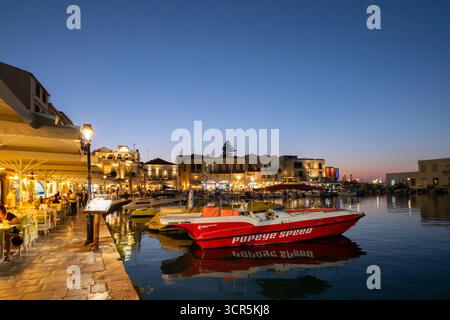 Rethymno, Creta. Una vista del vecchio porto nella città vecchia di Rethymnon al tramonto. Le luci illuminano i ristoranti e gli edifici intorno al vecchio porto Foto Stock