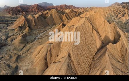 Vista aerea di aspre calanchi baciati dal sole che si estendono all'orizzonte, le loro vette erose che gettano ombre nette nel paesaggio arido, Ürümqi, Xinjiang, Cina. Foto Stock