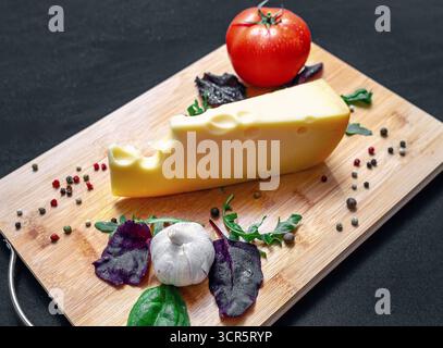 Un pezzo di formaggio su una tavola di legno. Set o assortimento di formaggi e verdure per un'alimentazione sana. Formaggio con insalata mista, pomodoro, aglio e pepe. BL Foto Stock