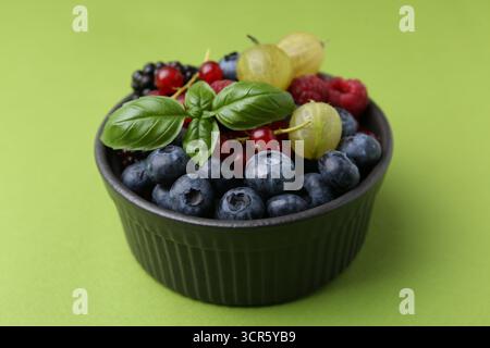 Diversi frutti di bosco e basilico maturi in ciotola su sfondo verde, primo piano Foto Stock