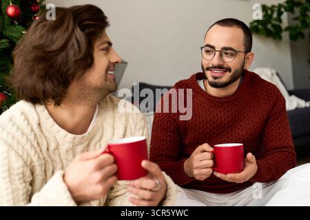 La coppia si diverte a bere qualcosa di caldo e a ridere nella propria allegra casa mentre celebra lo spirito natalizio. Foto Stock