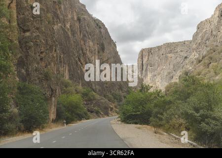Vista di una strada tortuosa e aspra che attraversa una gola spettacolare, le sue torreggianti pareti rocciose contrastano con il verde tenue del fogliame, Areni, provincia di Vayots Dzor, Armenia. Foto Stock