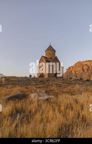 La vista del monastero medievale di Noravank si erge orgogliosamente sull'arido paesaggio, bagnato dal caldo bagliore del sole che tramonta, Areni, provincia di Vayots Dzor, Foto Stock