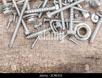 Dispositivi di fissaggio in metallo assortiti sparsi su una superficie in legno in un ambiente di officina Foto Stock