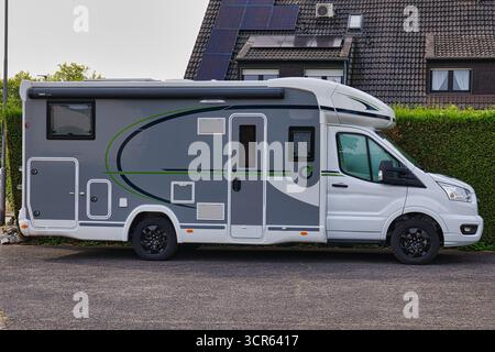 Moderno camper parcheggiato in strada vicino a case suburbane con pannelli solari Foto Stock