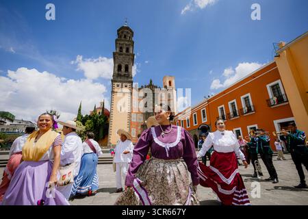 I ballerini messicani in colorati costumi folcloristici ballano in una piazza storica sotto un cielo blu, celebrando Huey Atlixcayotl a Puebla. Foto Stock