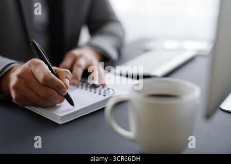 Primo piano di mans mani che prendono appunti sul posto di lavoro. Foto Stock