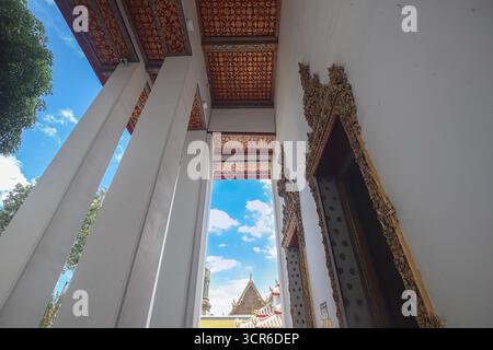 Vista dall'angolo basso del cancello del tempio Wat Pho a Bangkok. Soffitto decorato rosso e oro con porta scolpita incorniciata da cielo blu. Foto Stock