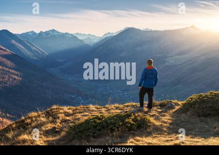 Giovane uomo in piedi su una cresta erbosa di montagna con vista sulla valle Foto Stock