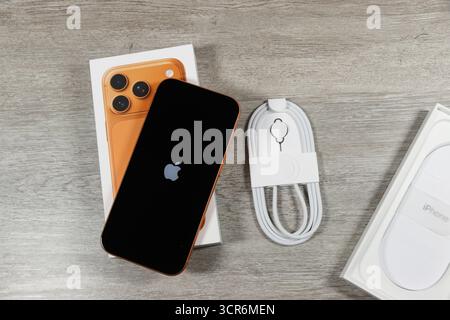 Nuovo smartphone iphone 17 Pro arancione con confezione, cavo di ricarica e accessori visualizzati su un tavolo di legno Foto Stock