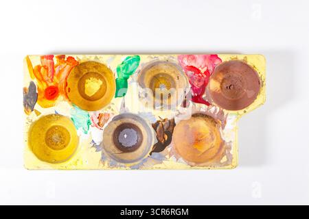 Vista dall'alto di una tavolozza di acquerelli usata con vari colori macchiati sul vassoio su uno sfondo bianco Foto Stock
