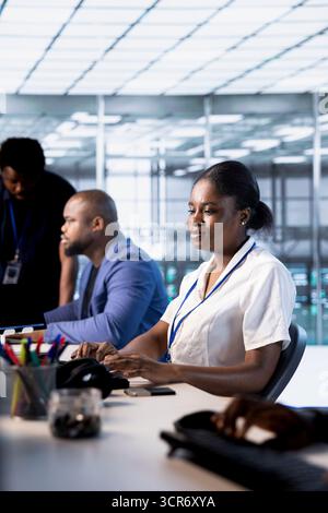 Tecnico afroamericano nel data center durante l'esecuzione di test diagnostici di sistema e utility di controllo degli errori. Donna accanto ai colleghi in cerca di problemi di rete che influiscono sulle prestazioni del server Foto Stock