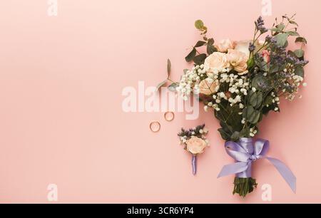 Bouquet e anelli da sposa esposti elegantemente su sfondo pastello Foto Stock