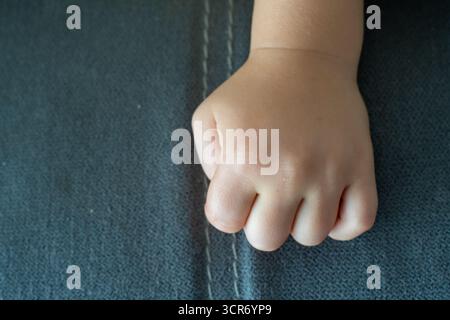 Titolo fotografico in inglese (200 caratteri): Primo piano della mano del paffuto del bambino e delle piccole dita appoggiate su una texture grigia. Concetto di sviluppo infantile, e. Foto Stock