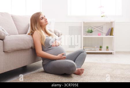 Donna incinta che si rilassa a casa mentre tiene la pancia durante il giorno Foto Stock
