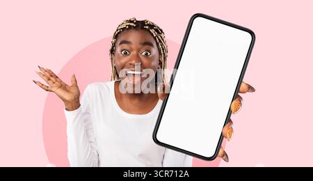 La giovane donna entusiasta tiene in mano uno smartphone con schermo vuoto su sfondo rosa per un uso creativo Foto Stock