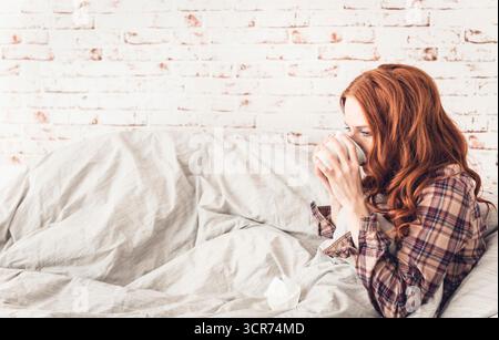 donna malata seduta sul divano a bere una tazza di tè Foto Stock