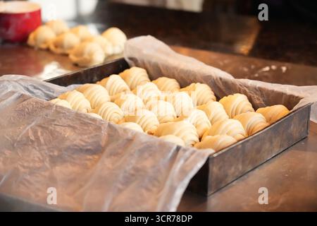 Croissant argentini crudi (medialunas) disposti su un vassoio da forno, pronti per essere cotti in una panetteria professionale. Impasto artigianale, preparato al momento, showcasi Foto Stock