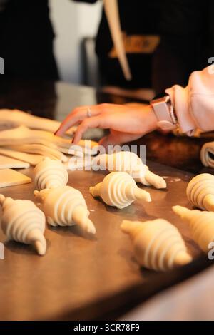 Croissant argentini crudi (medialunas) disposti su un vassoio da forno, pronti per essere cotti in una panetteria professionale. Impasto artigianale, preparato al momento, showcasi Foto Stock