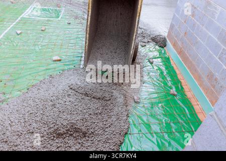 Il calcestruzzo bagnato viene versato dal camion sulla barriera al vapore verde nel cantiere per la flottazione Foto Stock