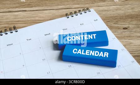 Informazioni sul calendario dei contenuti o sulla pianificazione della pubblicazione: Blocchi di legno blu con testo bianco su un calendario da scrivania su un tavolo da legno. Foto Stock