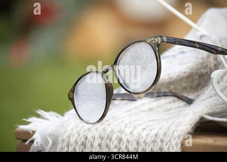Un paio di occhiali rotondi vintage si abbina a una sciarpa in lana testurizzata per catturare un momento di calma e sole all'aperto. Ideale per temi di stile, nostalgia e rela Foto Stock