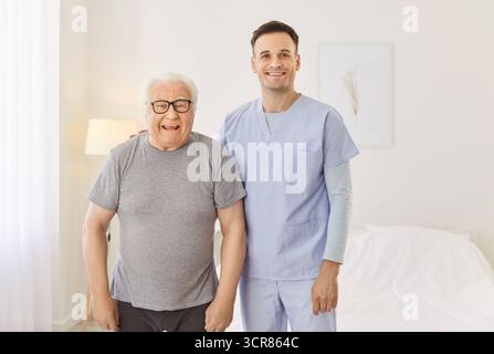 Ritratto di operatore sanitario felice con uomo anziano sorridente e abbracciato in clinica di riabilitazione Foto Stock