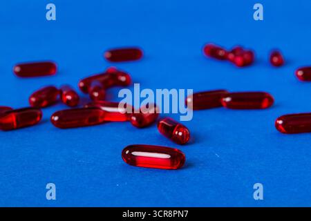 Mucchio di pillole rosse su sfondo colorato. Compresse sparse su un tavolo. Pila di capsule rosse di gelatina molle. Vitamine e supplementi dietetici concetto. Foto Stock
