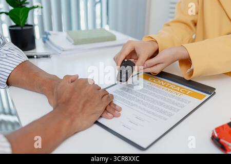 Una negoziazione per la vendita di auto si svolge in un ufficio in cui una donna venditrice con un blazer giallo spiega i dettagli di un contratto a un cliente maschio, showin Foto Stock