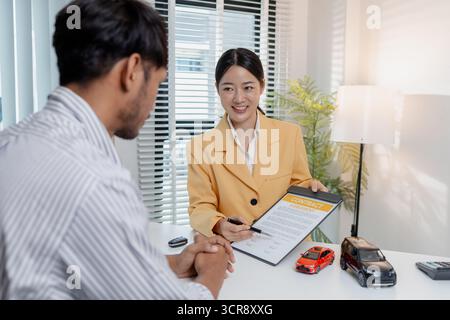Una negoziazione per la vendita di auto si svolge in un ufficio in cui una donna venditrice con un blazer giallo spiega i dettagli di un contratto a un cliente maschio, showin Foto Stock