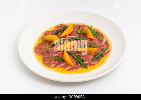 Carpaccio di manzo a fette sottili con segmenti di arancia e foglie di rucola Foto Stock