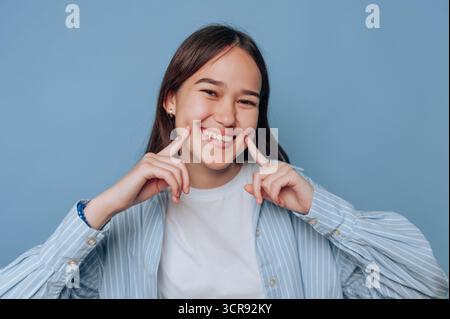ritratto di una giovane donna allegra che sorride ampiamente su sfondo azzurro Foto Stock