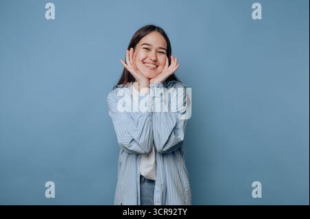 la giovane donna posa gioiosamente, mostrando la sua vibrante personalità con un sorriso luminoso su sfondo azzurro Foto Stock