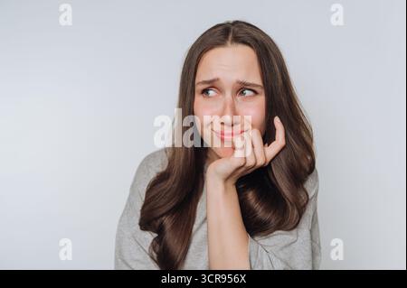 la giovane donna mostra un'espressione preoccupata, esprimendo in modo candido i suoi pensieri interiori e i sentimenti di ansia o preoccupazione sottostanti su sfondo bianco Foto Stock