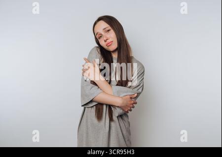 la giovane donna pensiva si trova in una posa premurosa, incarnando la vulnerabilità su sfondo bianco Foto Stock